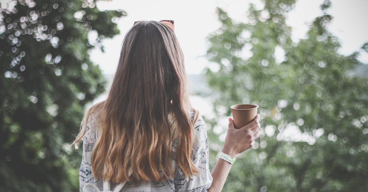 back of a woman outside, holding coffee