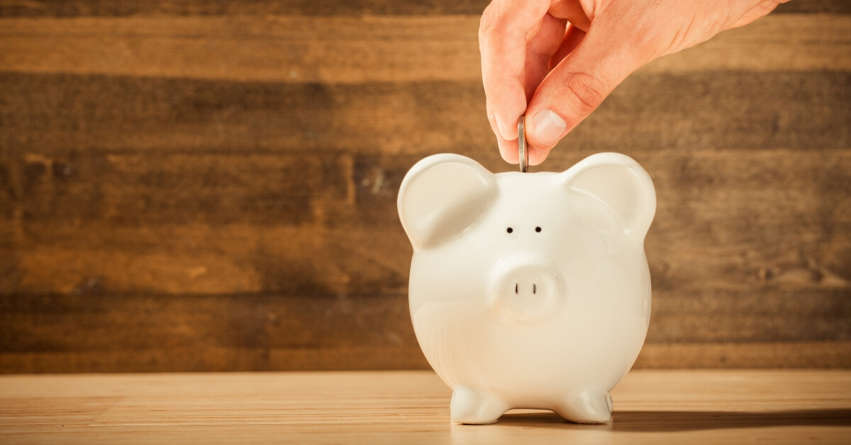 a hand putting a coin into a piggy bank