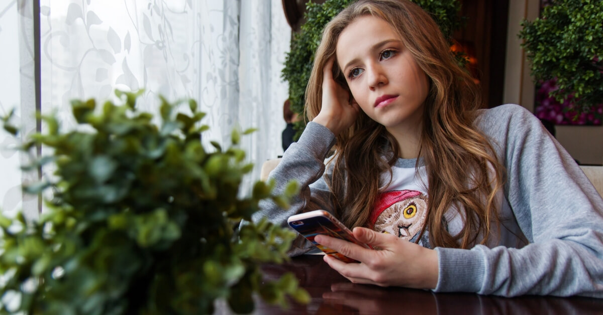 a girl with a phone in her hand gazing into space