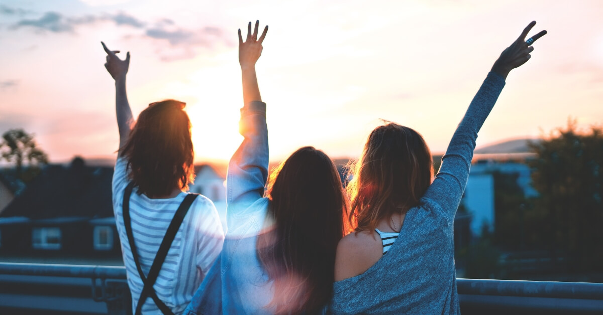 three girls with their backs turned with arms in the air