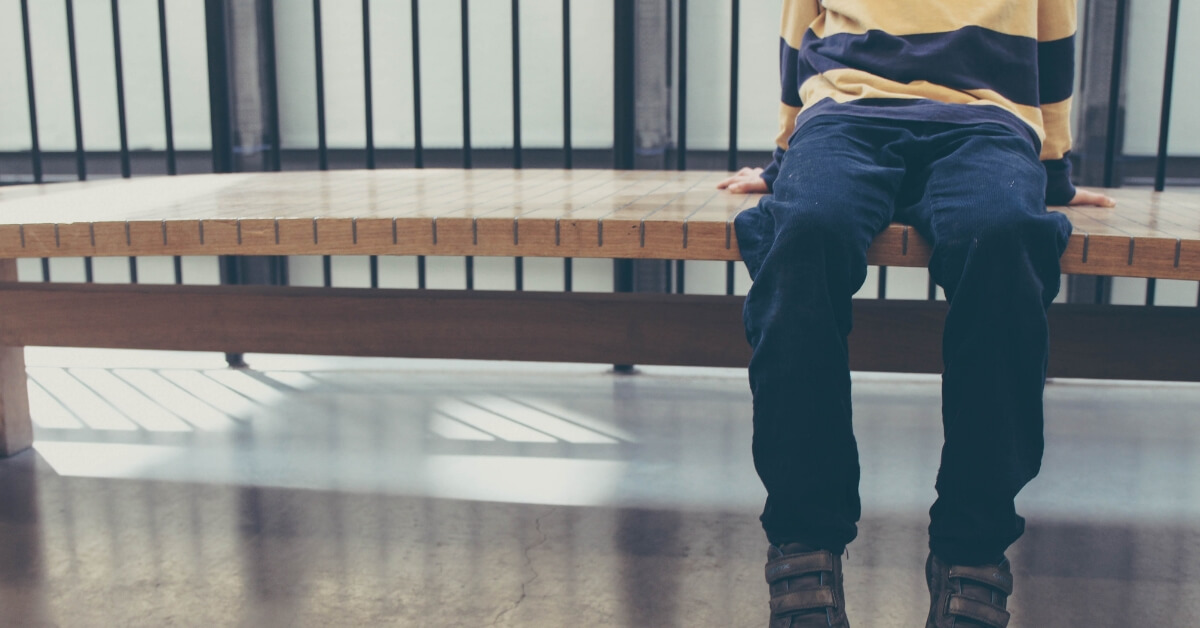 torso and legs of a young boy sitting on a bench