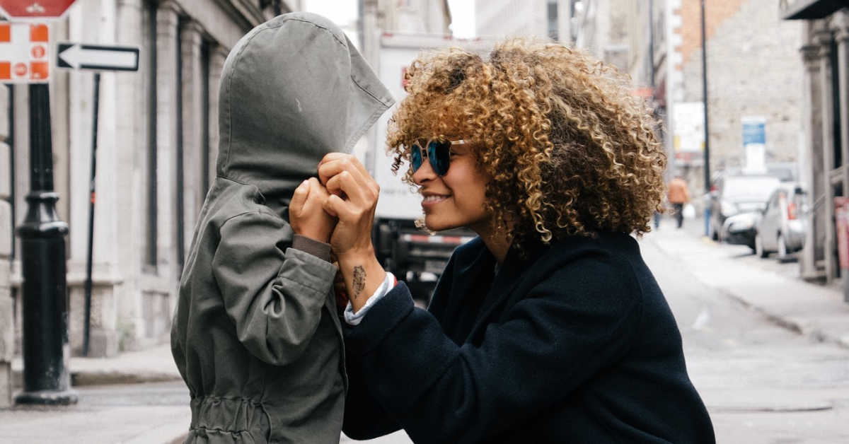 Mum kneeling next to child smiling and pulling on hoodie