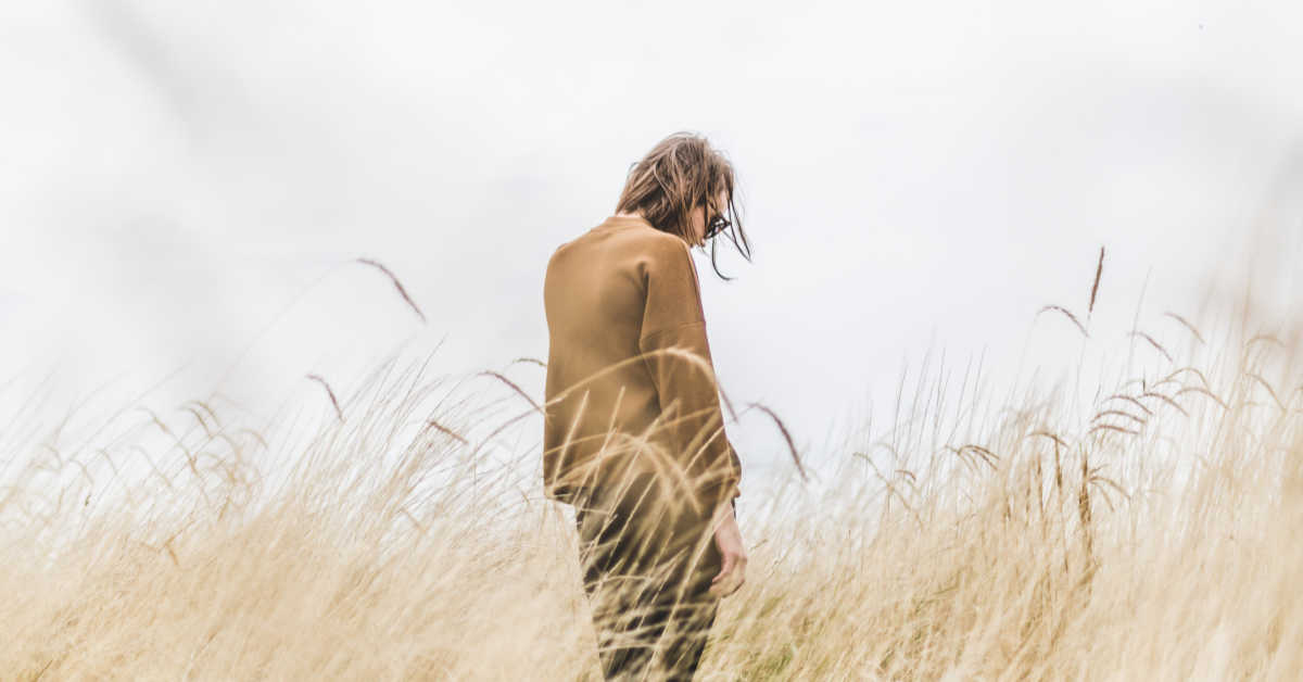 Person standing alone in field looking down