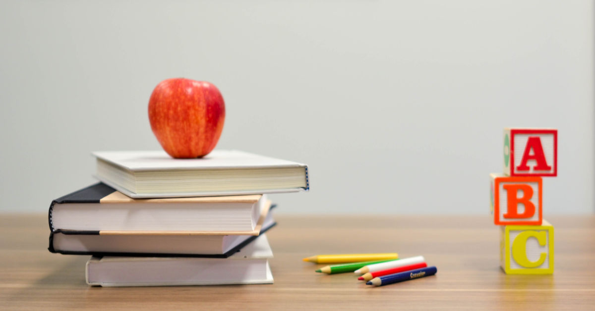 Apple on top of school books and pencils on the side of the desk