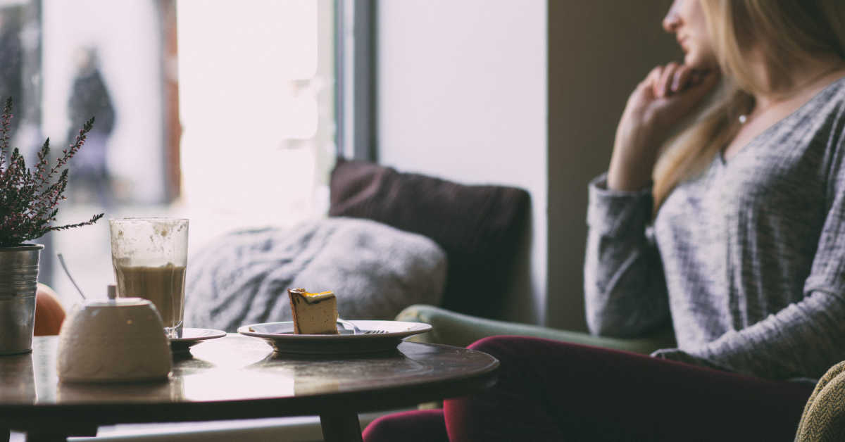 woman sitting at coffee table with half finished cake on table looking out the window