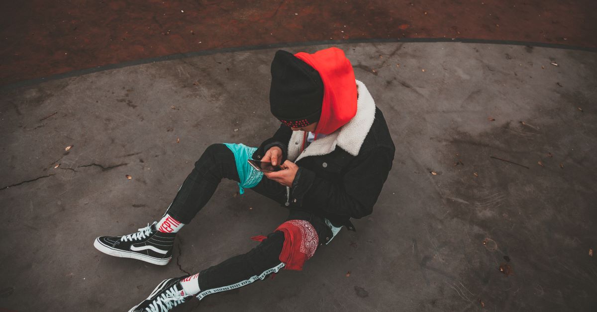 teen looking down at phone while sitting on ground