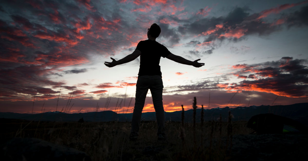 Person lifting their hands to the sky at sunset