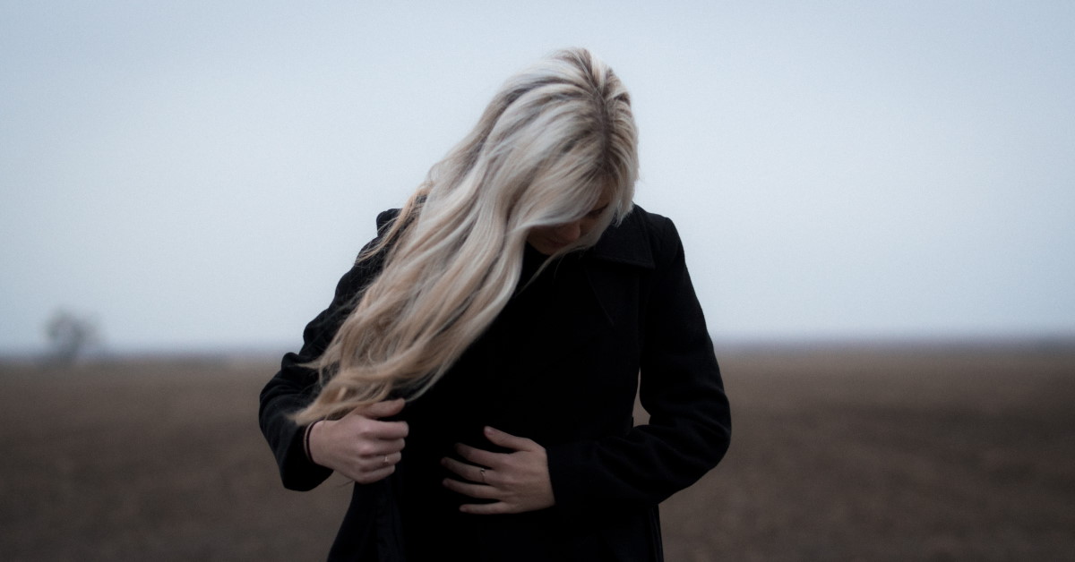 Woman walking in field wearing coat with hand on stomach