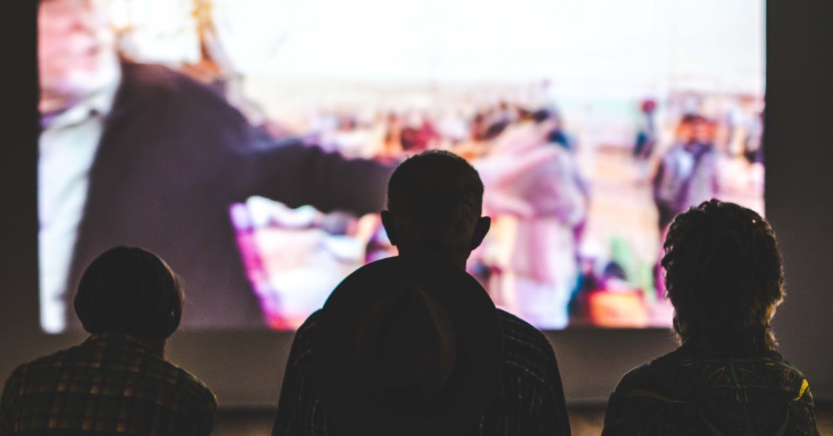 Silhouettes of people watching images on a big screen