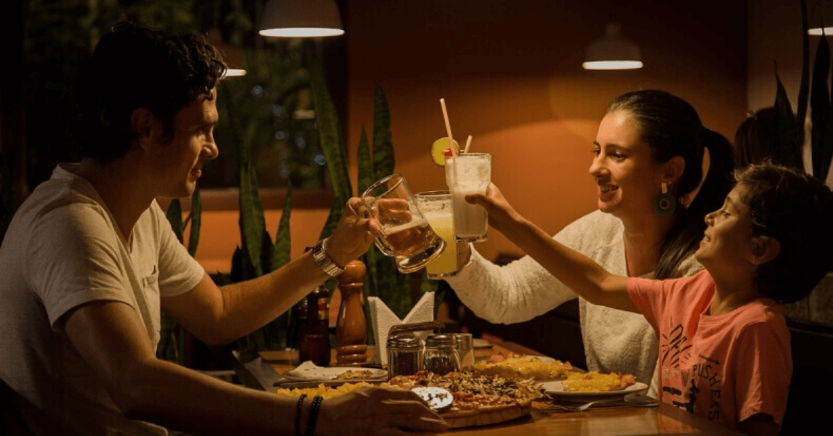 family of 3 around a dinner table smiling and clinking glasses