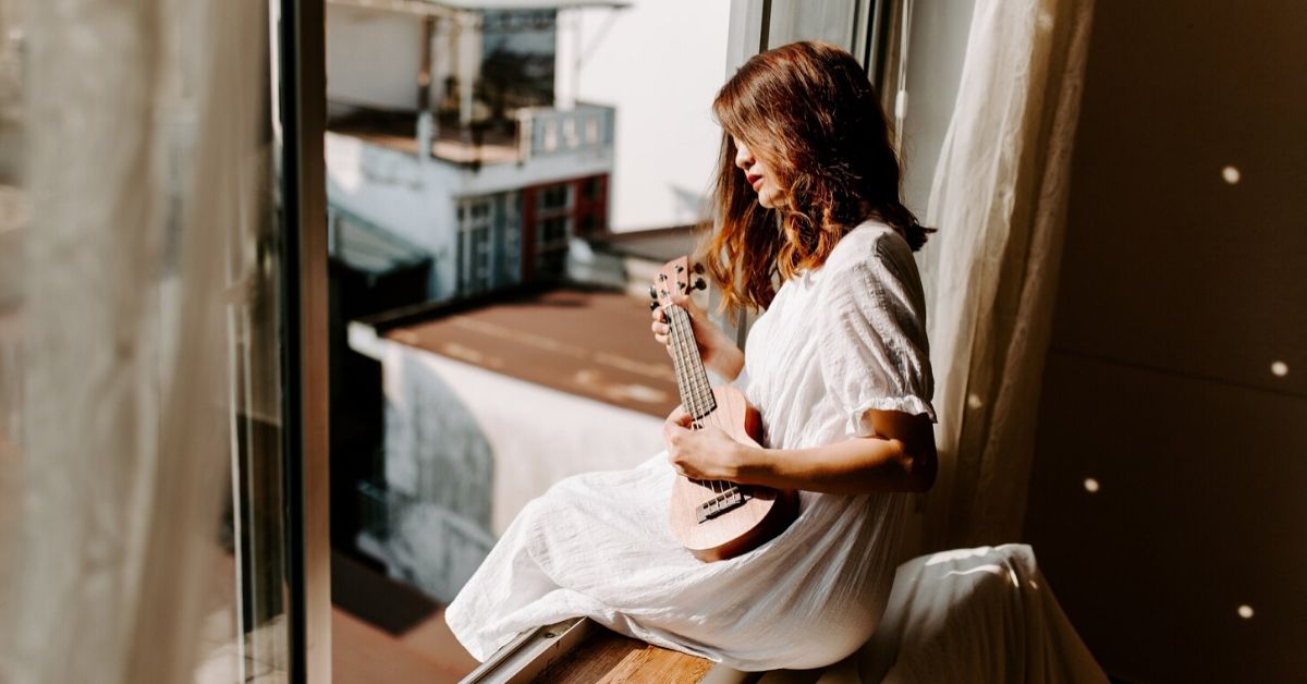 photo of woman playing ukelele sitting on a window frame