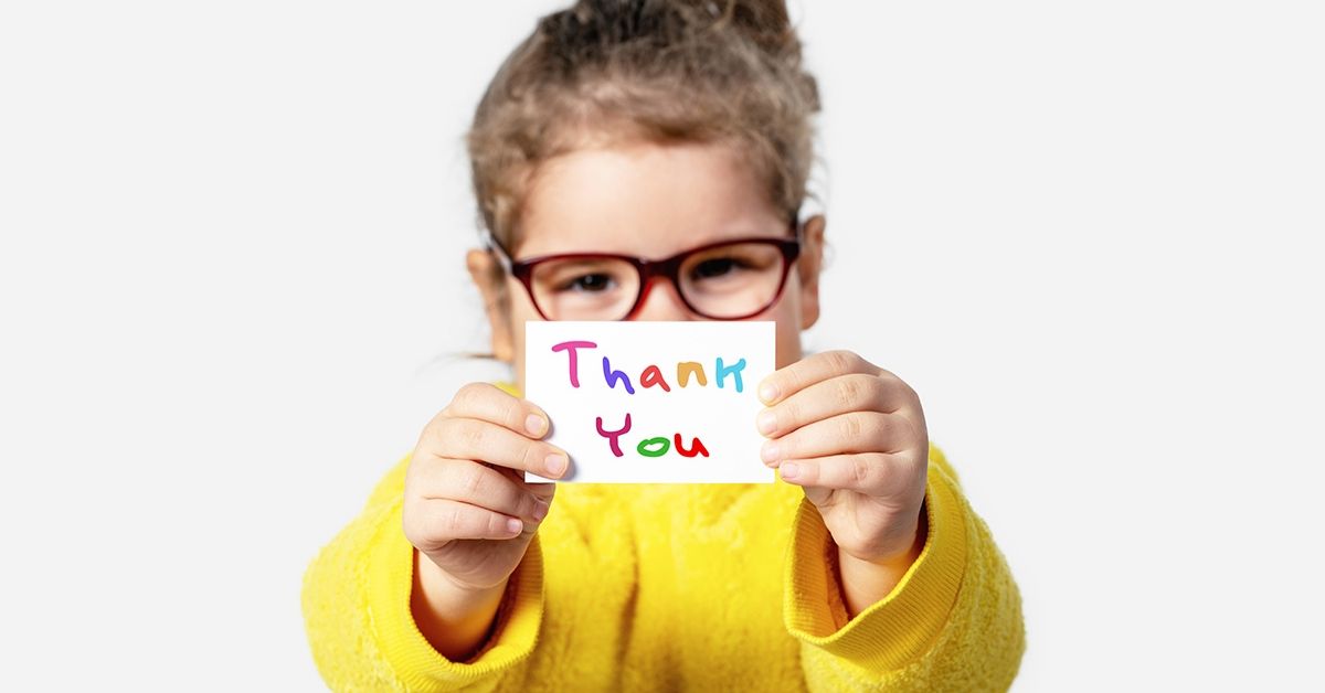 photo of a young girl holding a paper in front of her which says thank "thank you" in colourful letters.