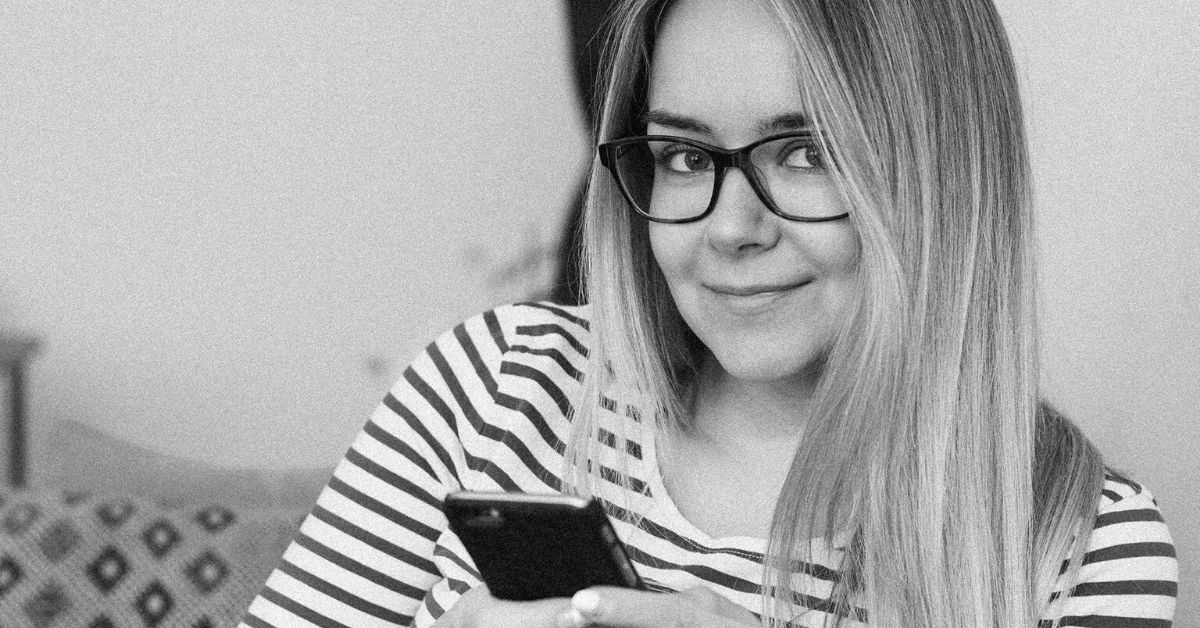 black and white photo of a girl holding her phone smiling at the camera