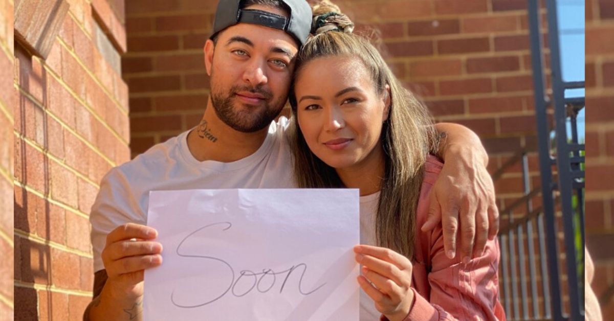 A photo of singer chris sebastian and his wife tash sittg on stairs holding a paper with soon written on it