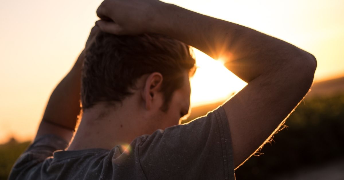 man looking down with hands interlocked on his head