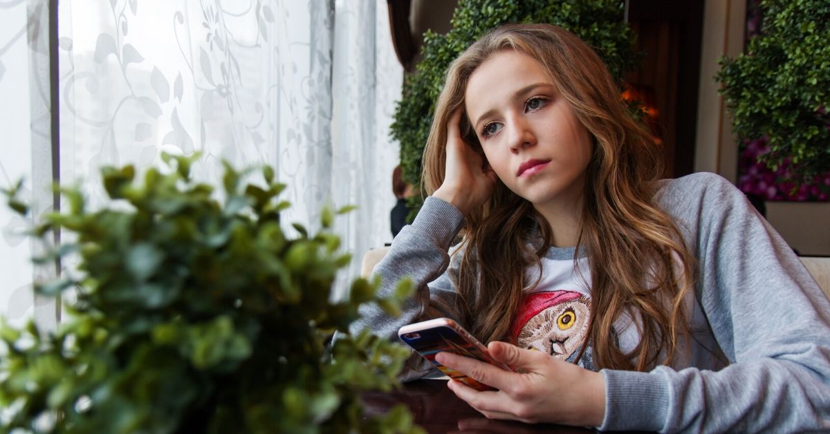 photo of a teen holding a phone gazing out the window