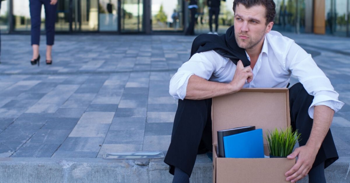 photo of a well dressed man sitting on the side of the road wth a box of belongings