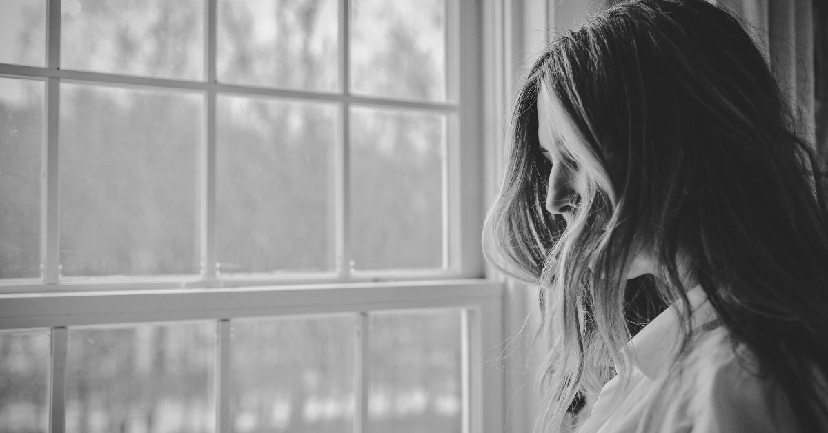 black and white photo shows a woman standing at a window with hair covering her face