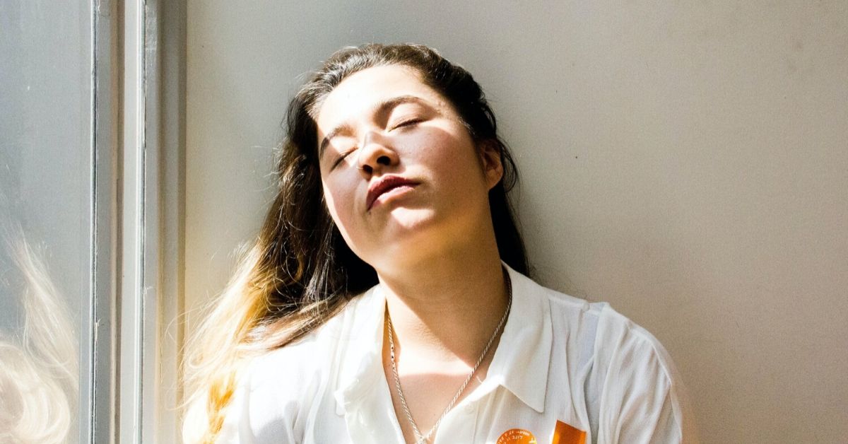 girl with eyes closed leaning against a wall as sunlight spills over her face