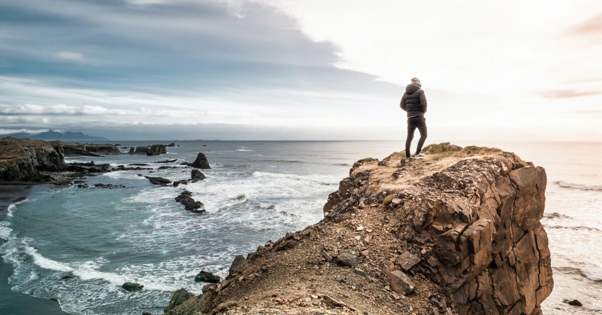 man standing on a hill overlooking the ocean