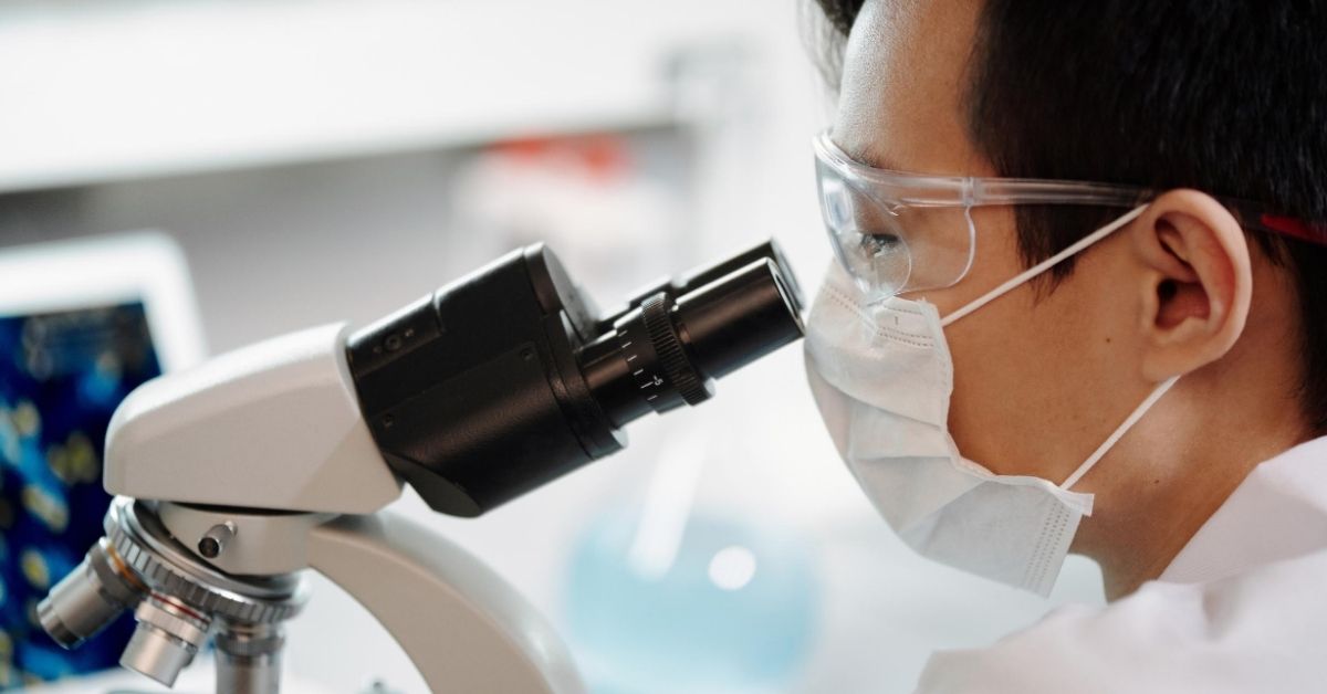 man wearing mask look through a microscope in laboratory