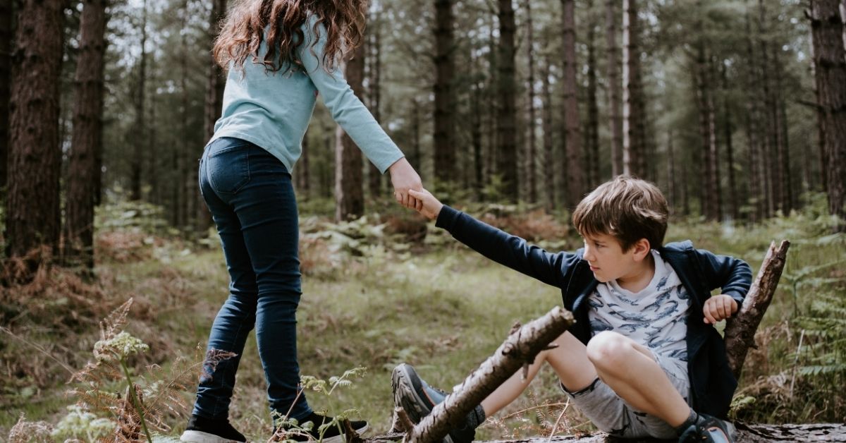 a girl helps a boy who has fallen down