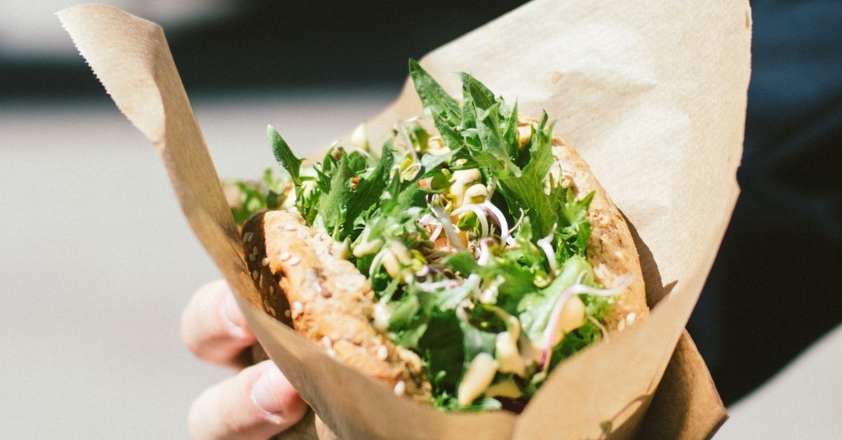 a person holds a sandwich wrapped in brown paper on the street