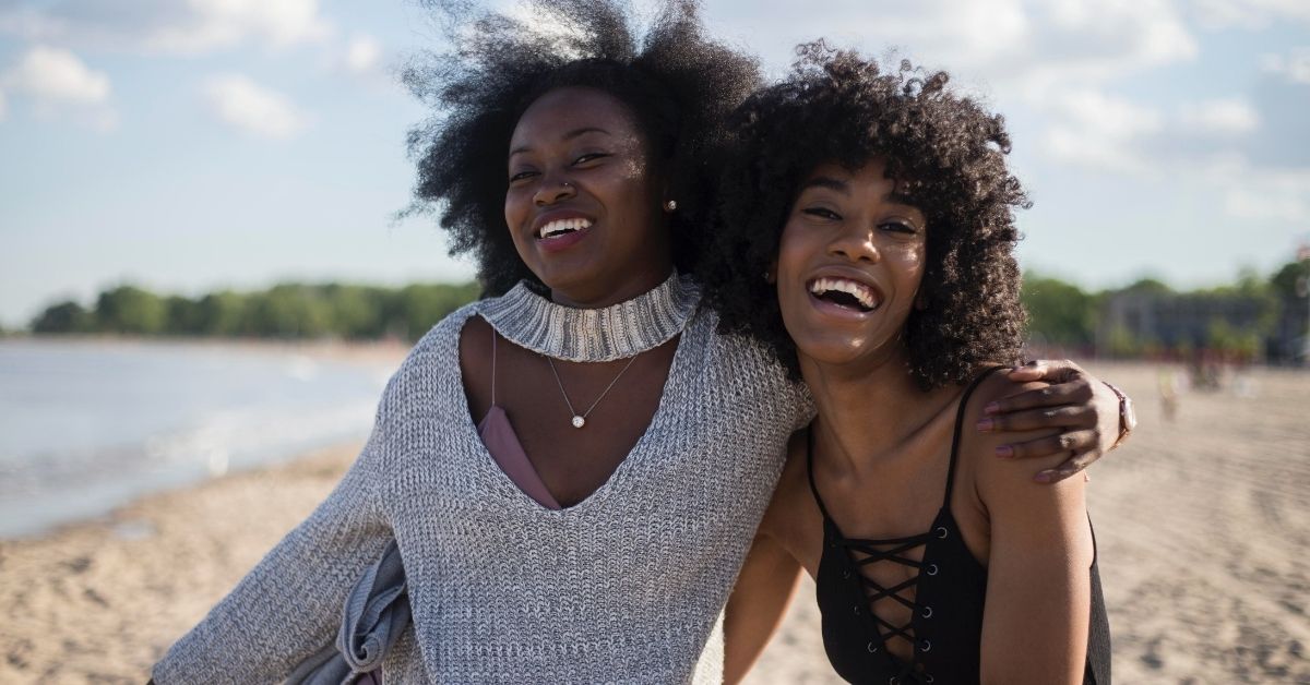 two friends with arms around each other laughing at the beach