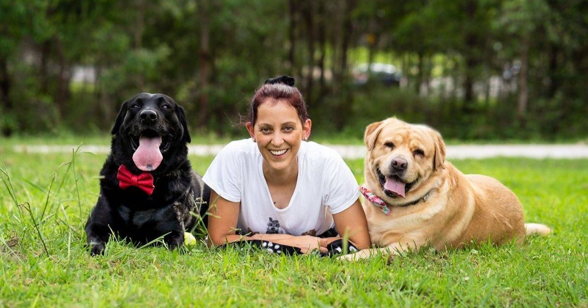 bianca smiling laying on grass with a dog on each side