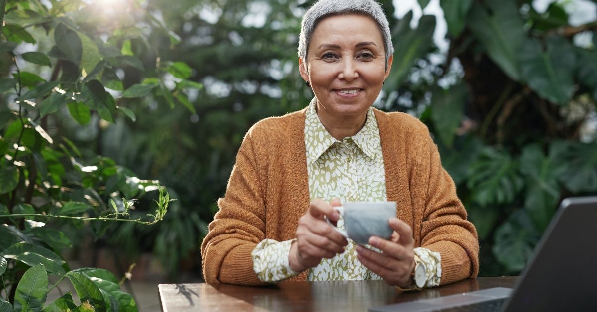 woman sits at an outdoor table with laptop and cup of tea