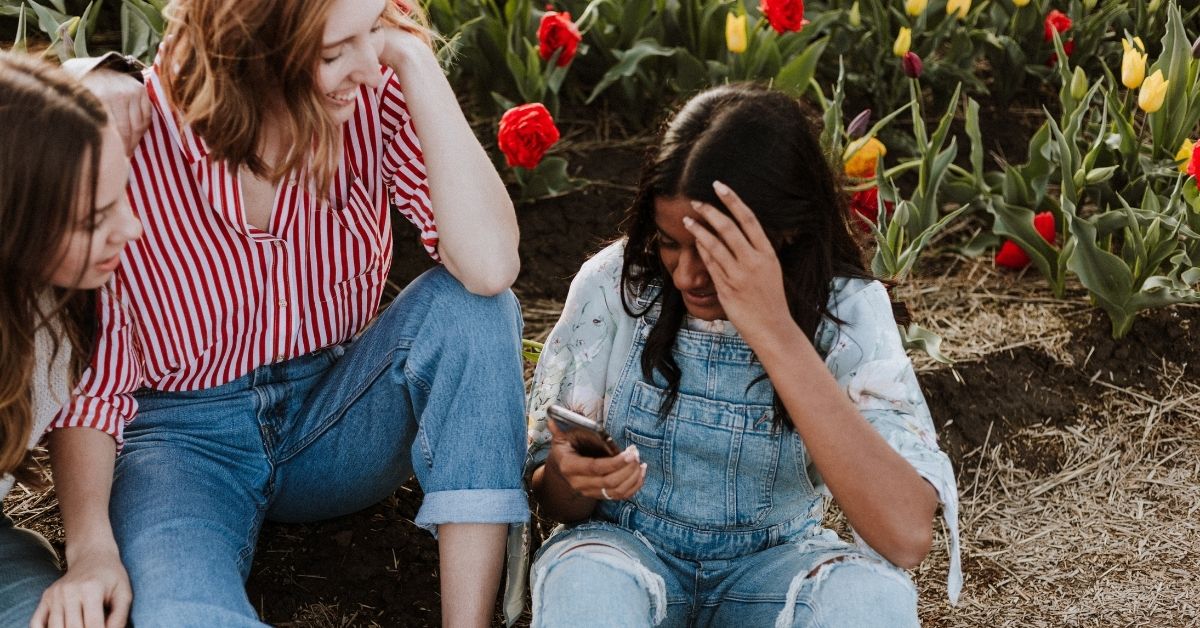 a group of friends sit on the ground together looking down at a phone