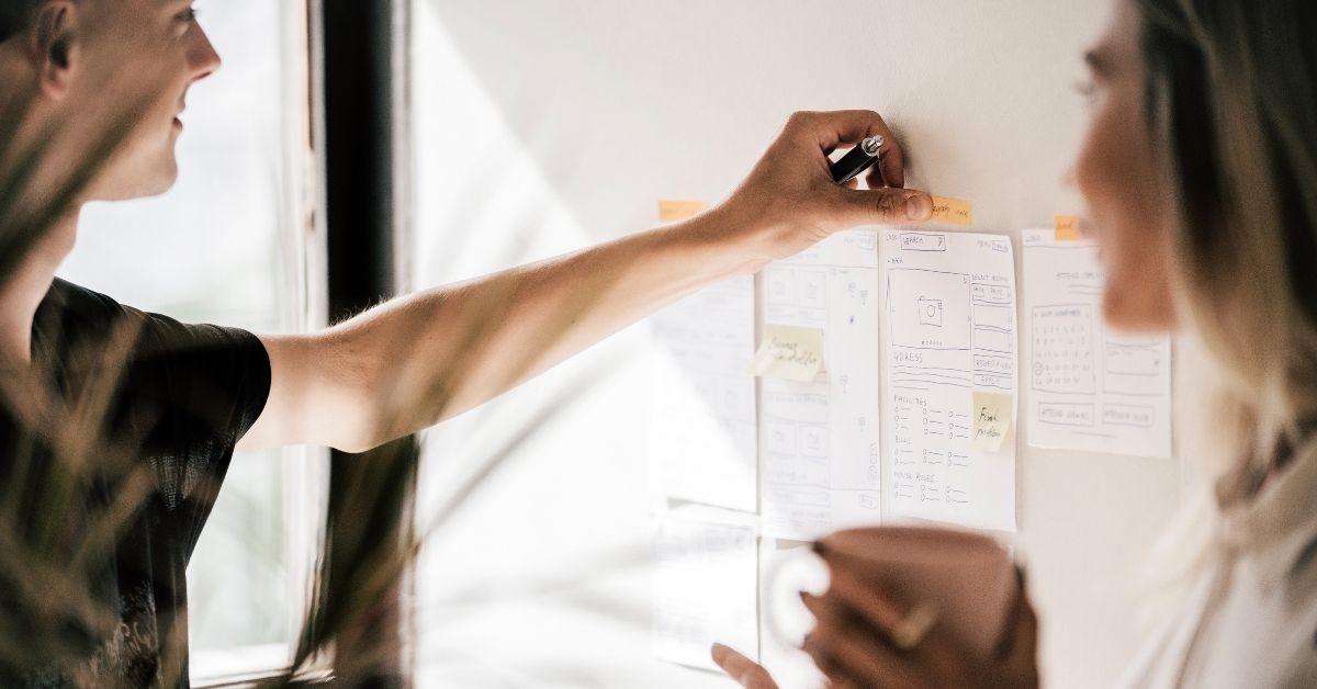 two coworkers examine sticky notes on a collaborative whiteboard