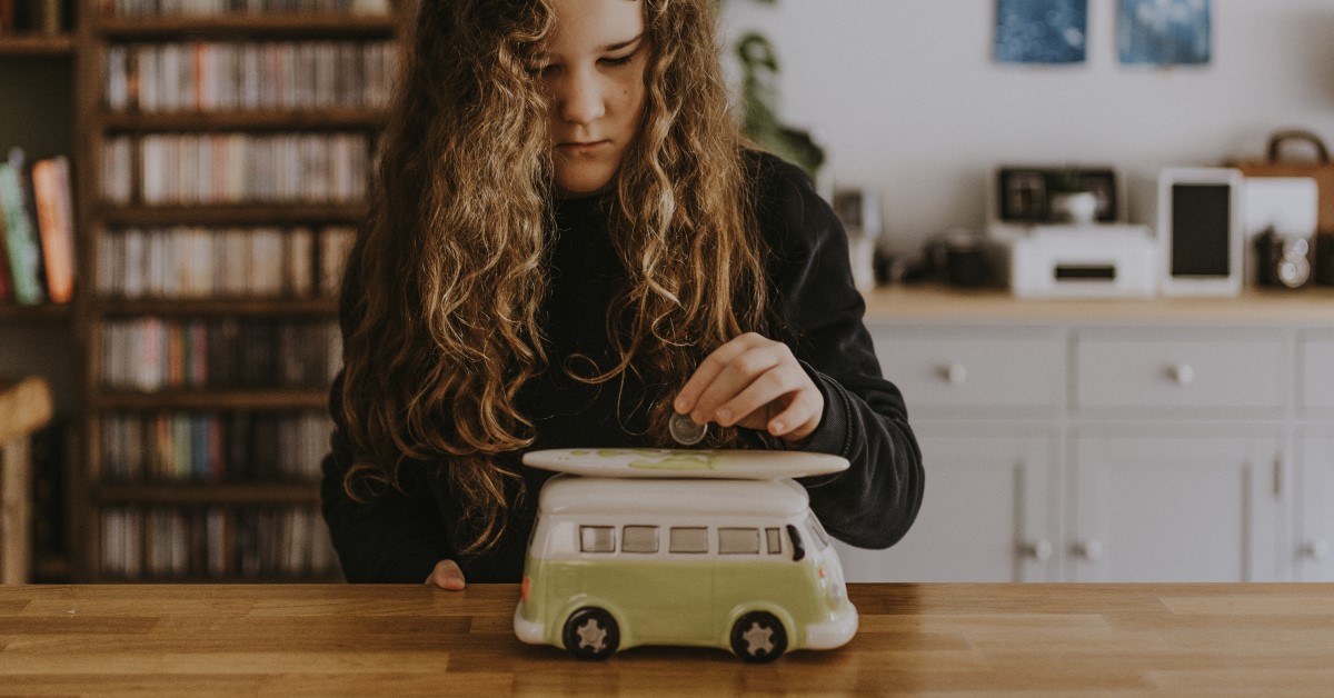 Tween girl putting coin into money box that looks like a combie van with a surfboard on top