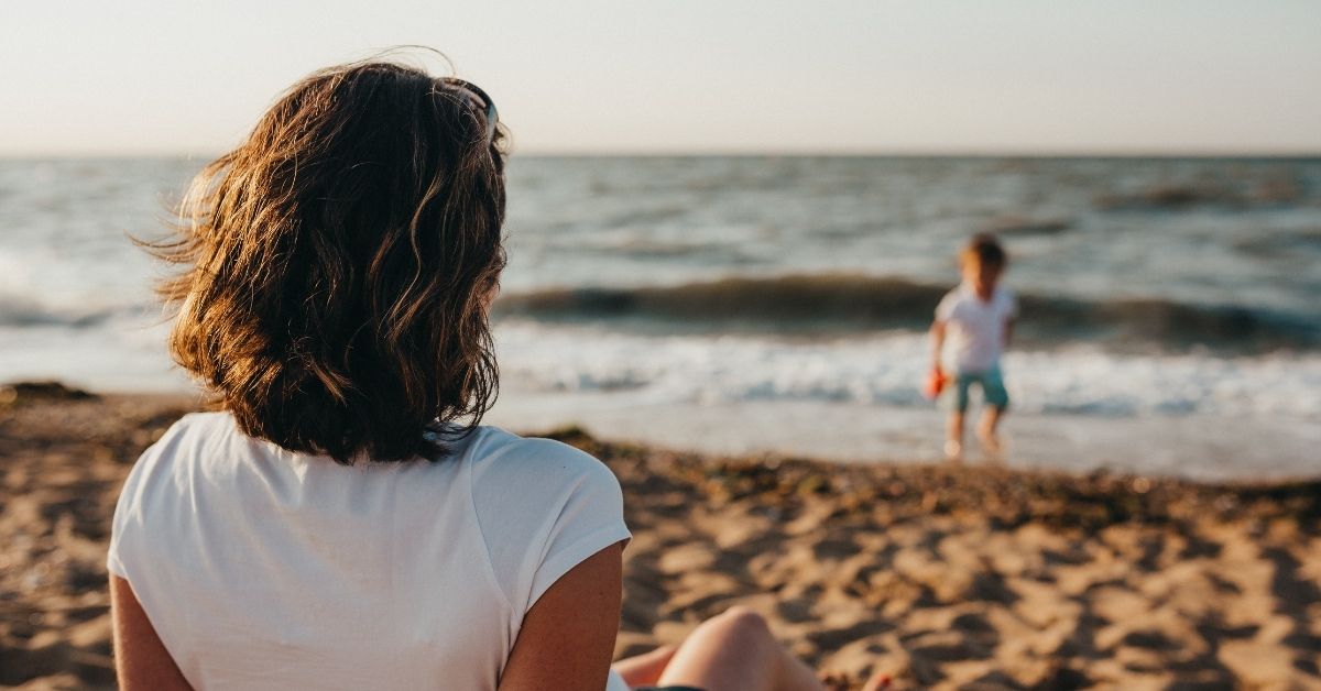 a mum watches her son play at the beach