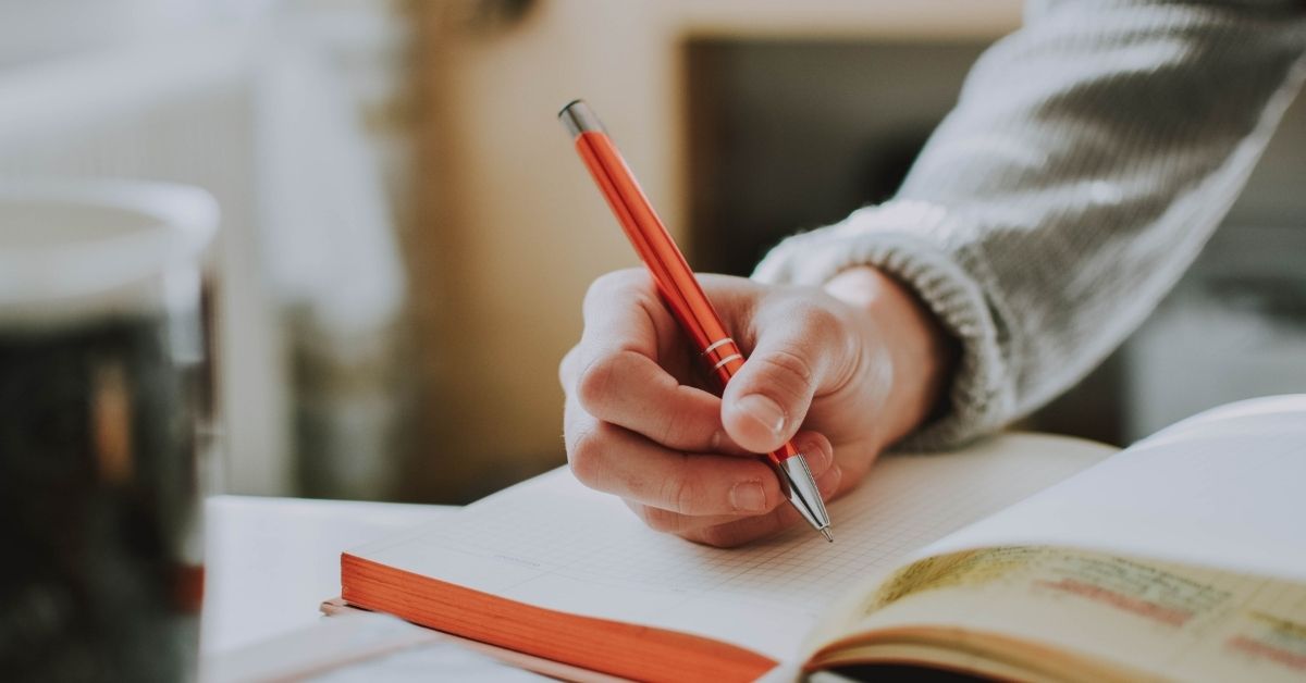 a woman writes in a journal with a red pen