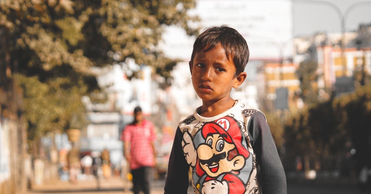 a young boy of middle eastern appearance stands in a street