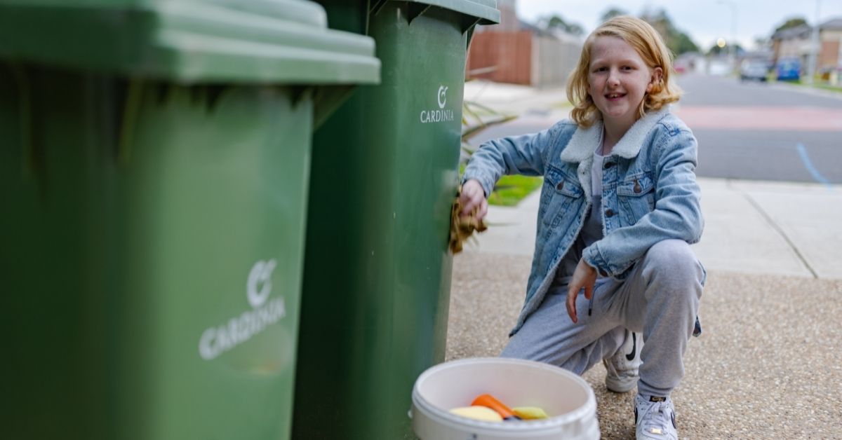 curtis with cleaning supplies kneeling bside two green wheelie bins