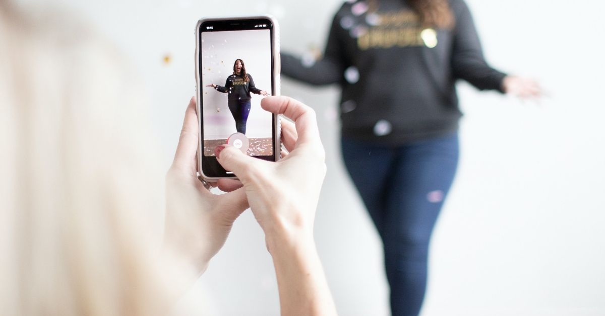 a girl takes a video of her friend throwing confetti in the air