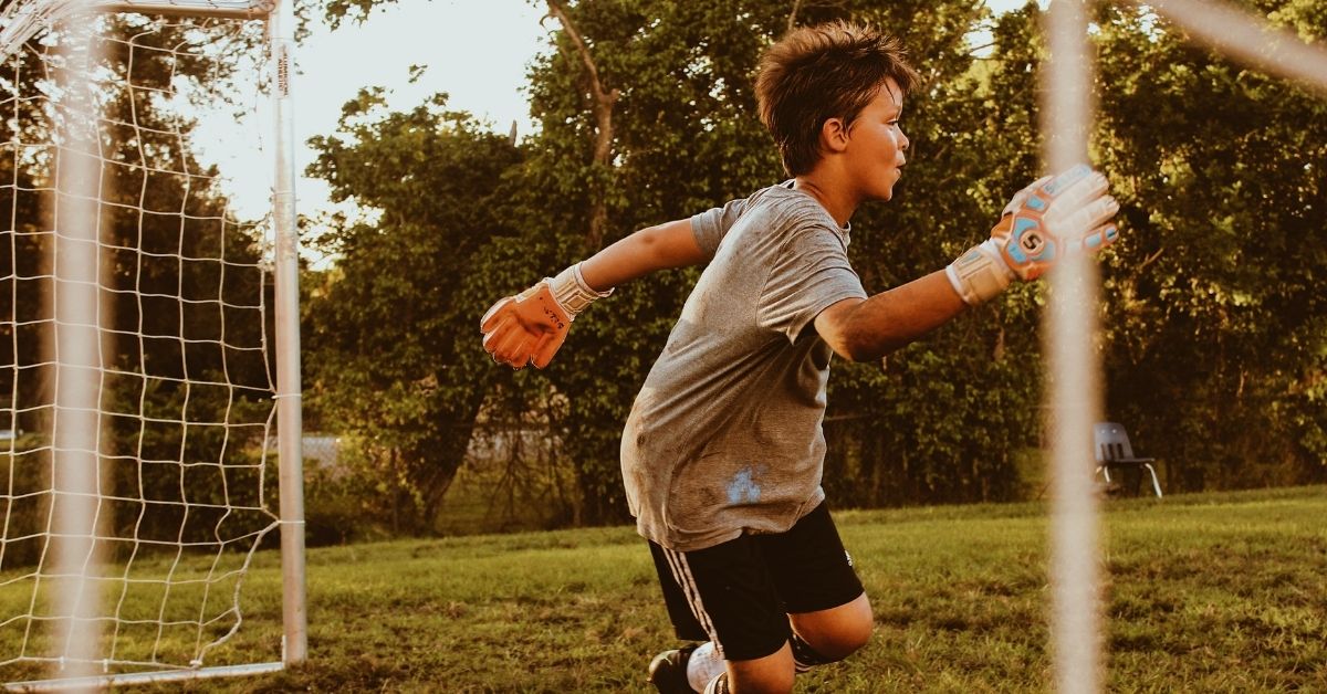 a boy playing as a goalie in soccer runs to block a ball