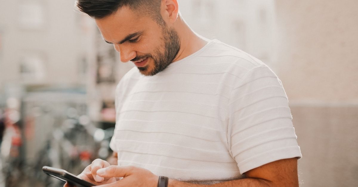 man in a white shirt looks down as he types on his phone