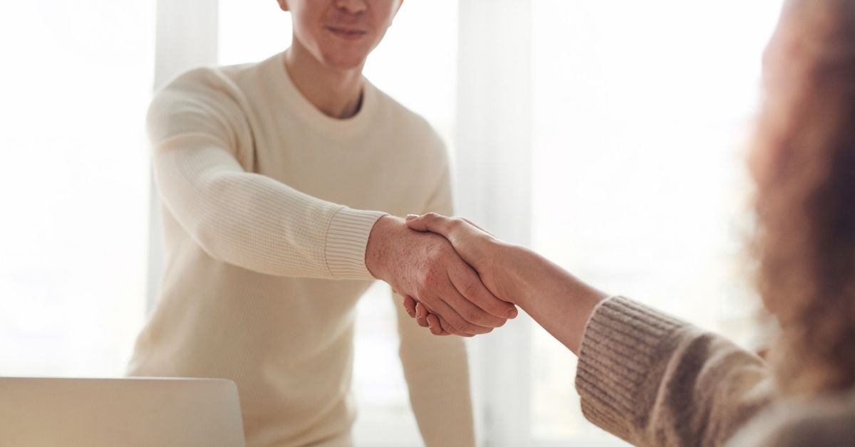 a man shakes a woman's hand over a meeting room table in a job interview