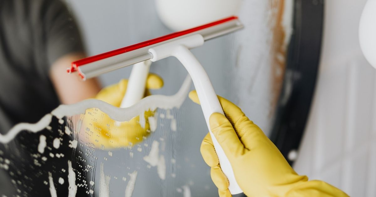 a person wearing a yellow glove uses a squeegee on a mirror