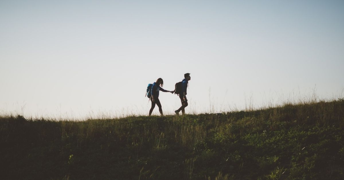 a silhouette of a person leading another by the hand up a hill