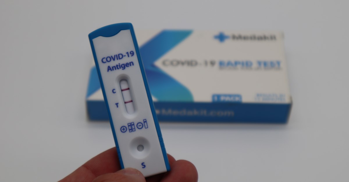 hand holding postive COVID RA Test with RA packet in background